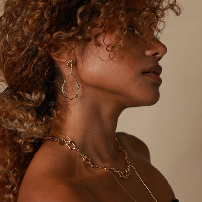 Close-up of a person wearing gold hoop earrings and a necklace against a neutral background
