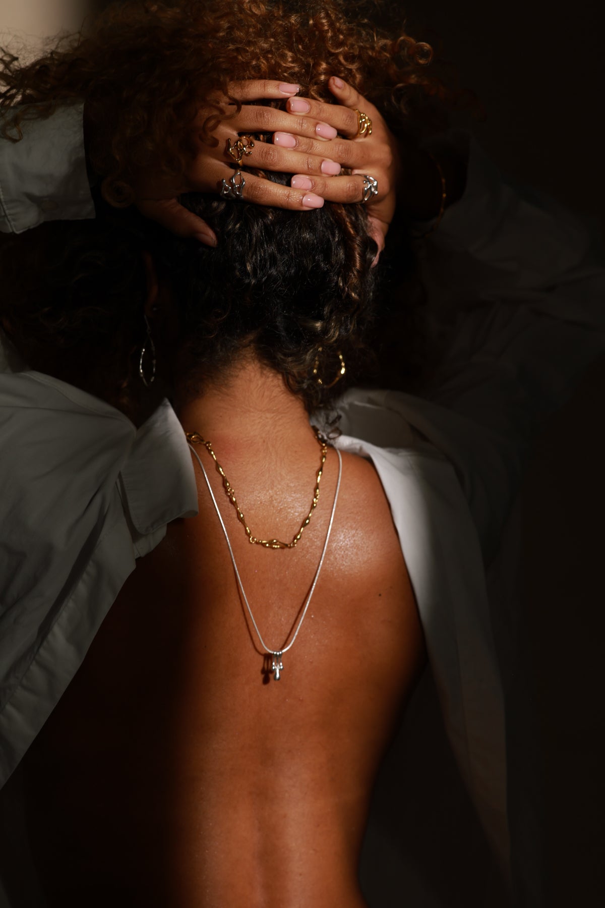 Person wearing gold necklaces by JYOCO with a dark background