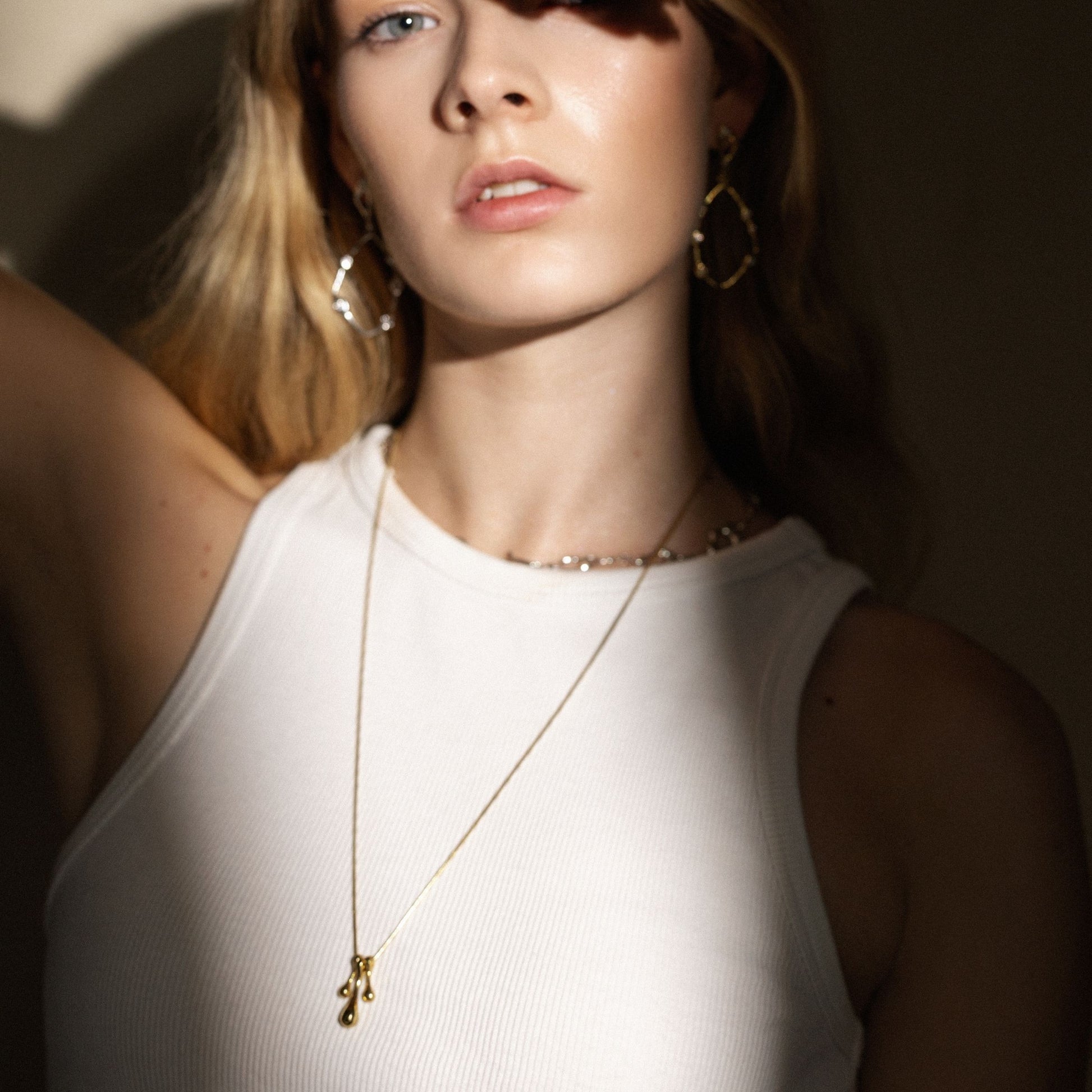 Woman wearing a gold necklace and hoop earrings with a neutral background