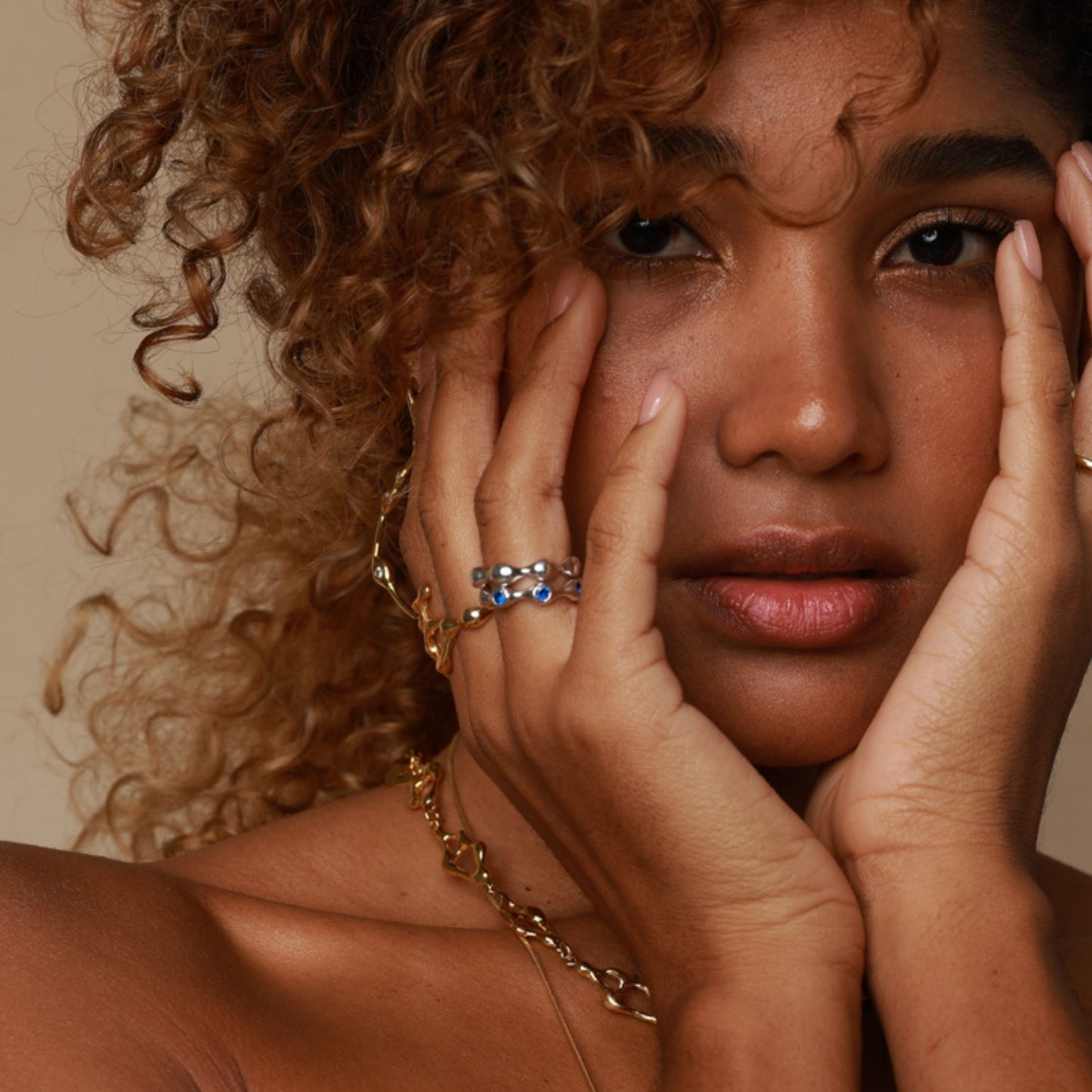 Woman with curly hair wearing gold jewelry against a neutral background