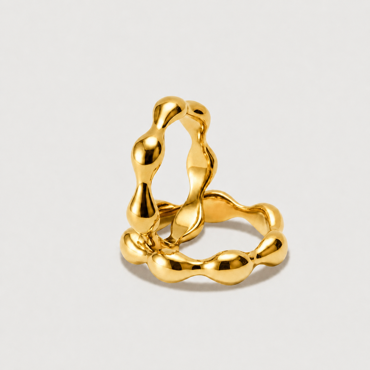 Gold ring with a unique, wavy design on a light gray background