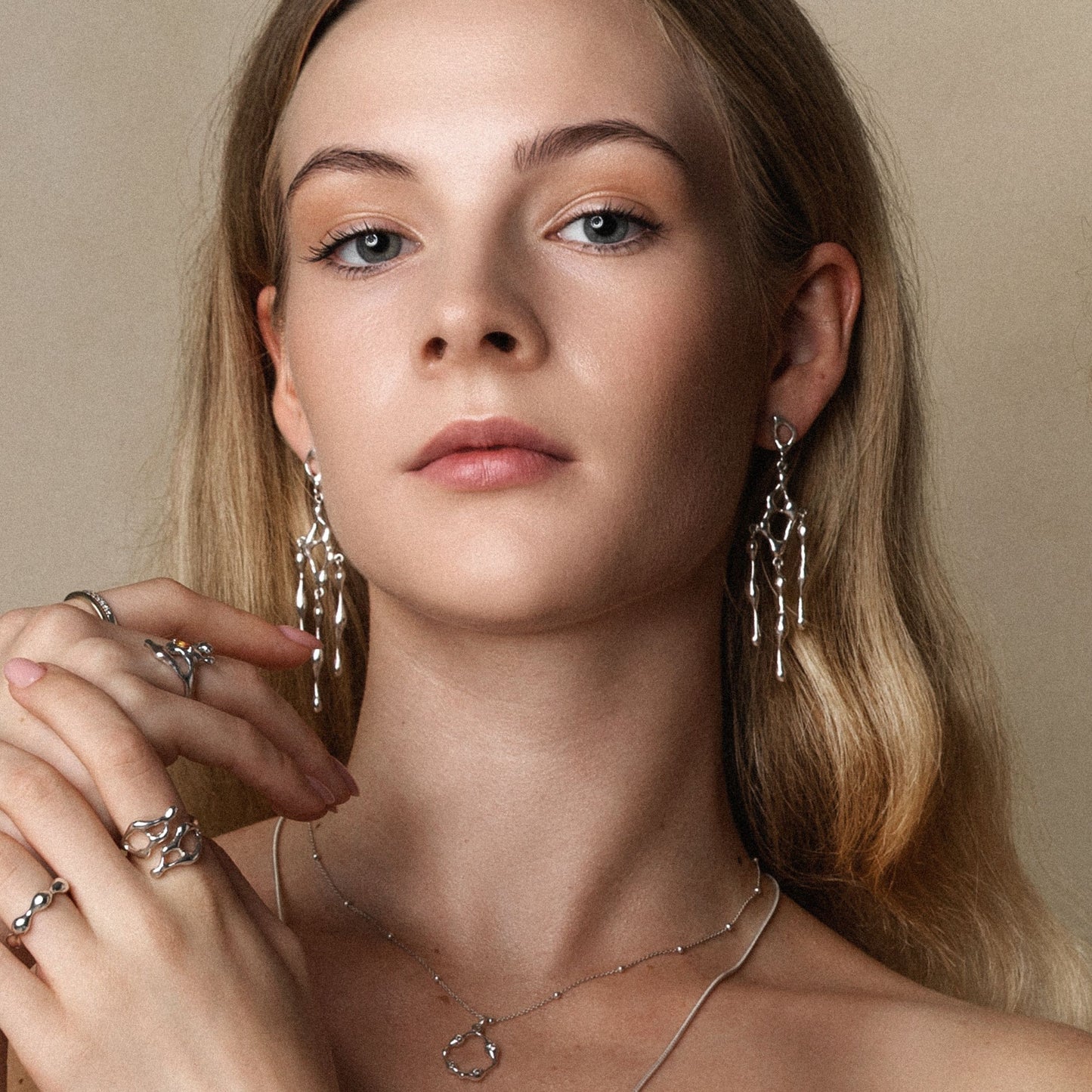 Woman wearing silver jewelry including earrings and rings against a neutral background