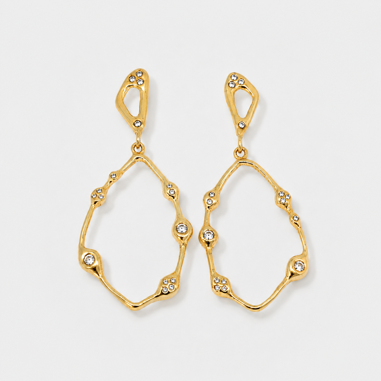 Gold earrings with diamond-like stones on a light gray background