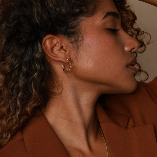 Close-up of a person wearing gold hoop earrings with a warm-toned background