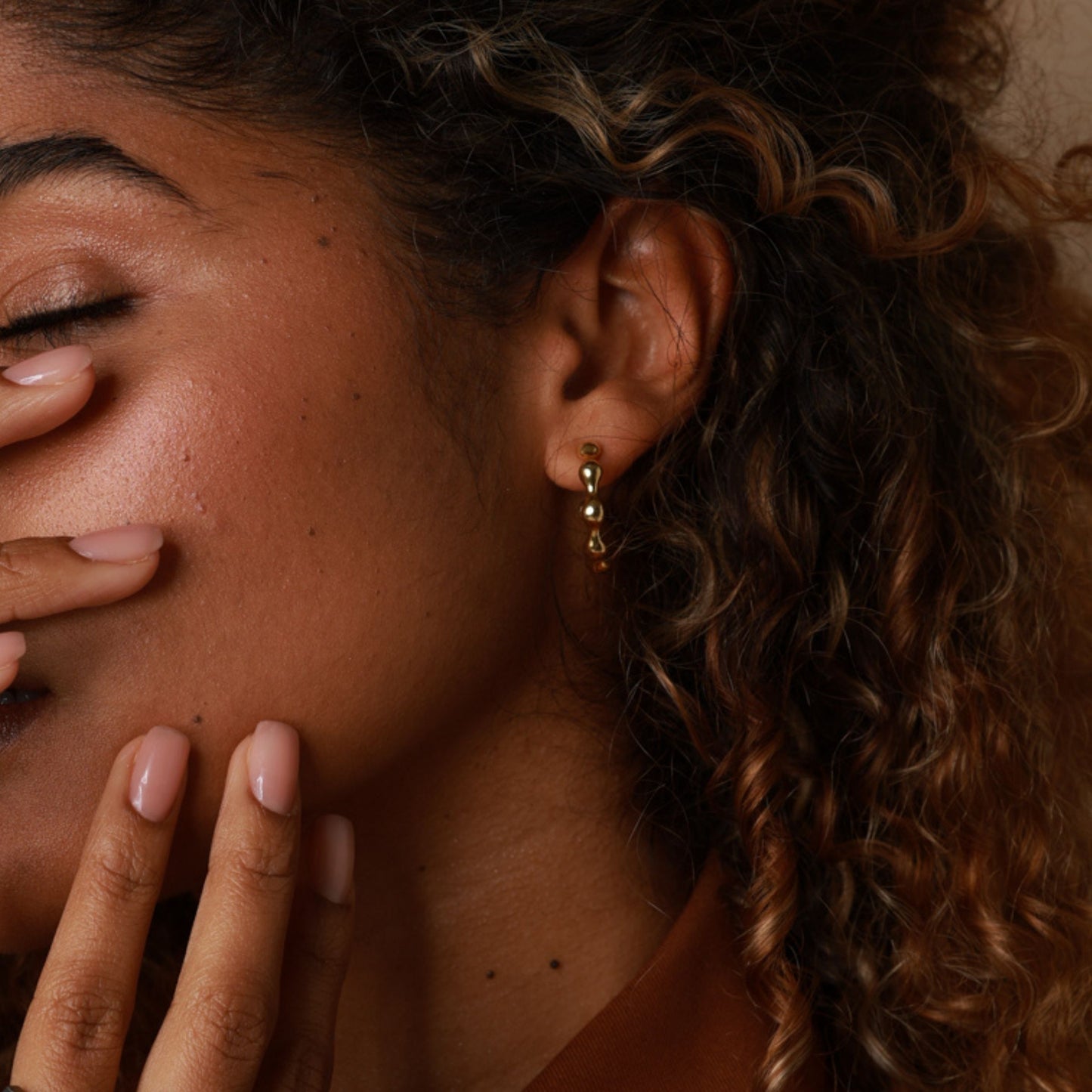 Close-up of a woman's face with a hand covering her mouth, wearing gold earrings.