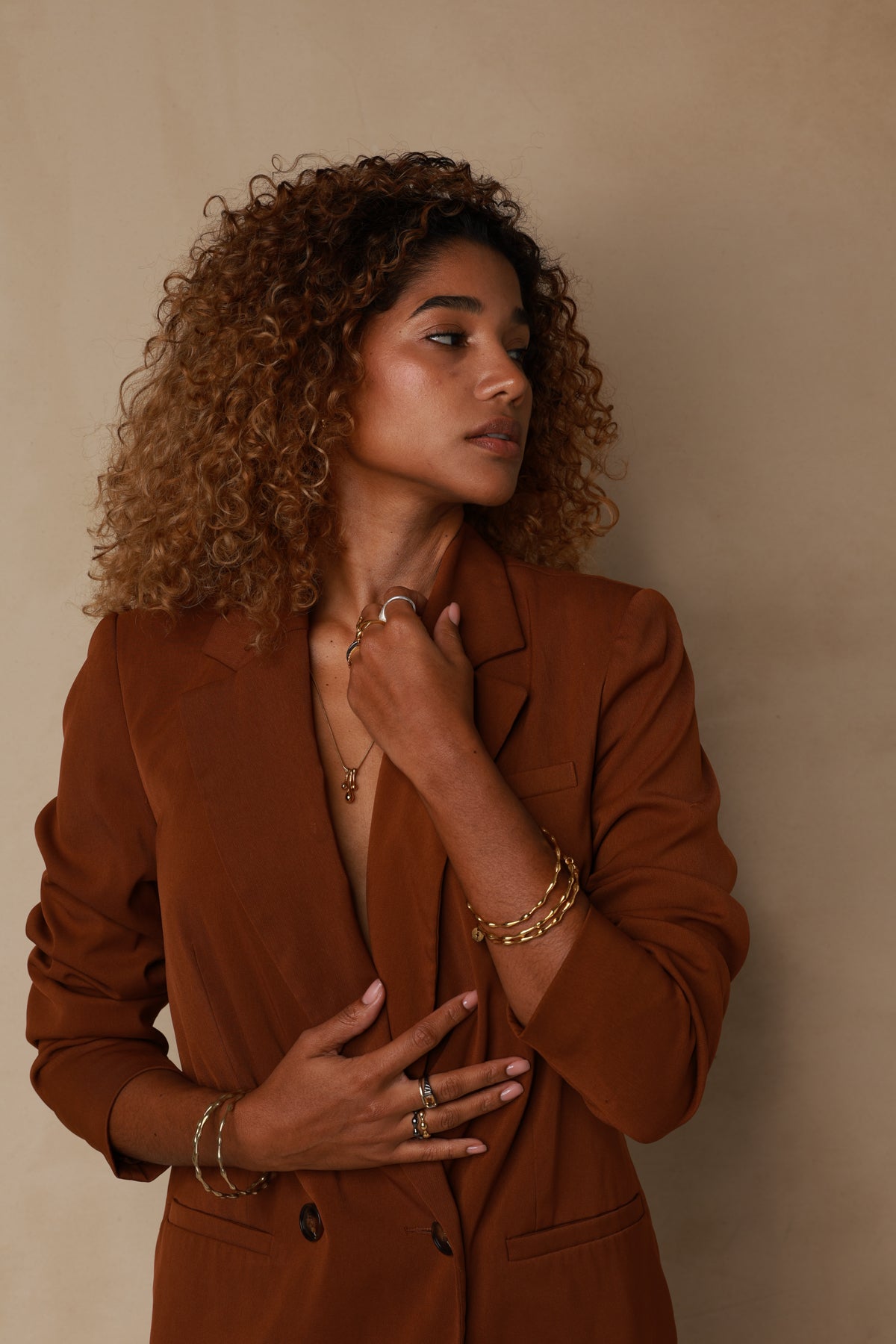 Woman in a brown suit with jewelry against a beige background