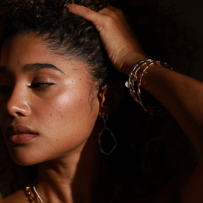 Woman with hand adjusting her hair, wearing a bracelet, in a warm-toned setting