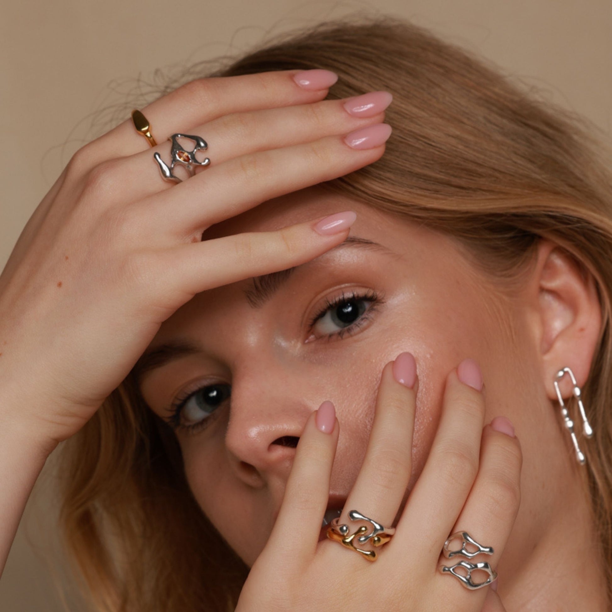 Close-up of a woman's face with hands covering her face, wearing multiple rings.