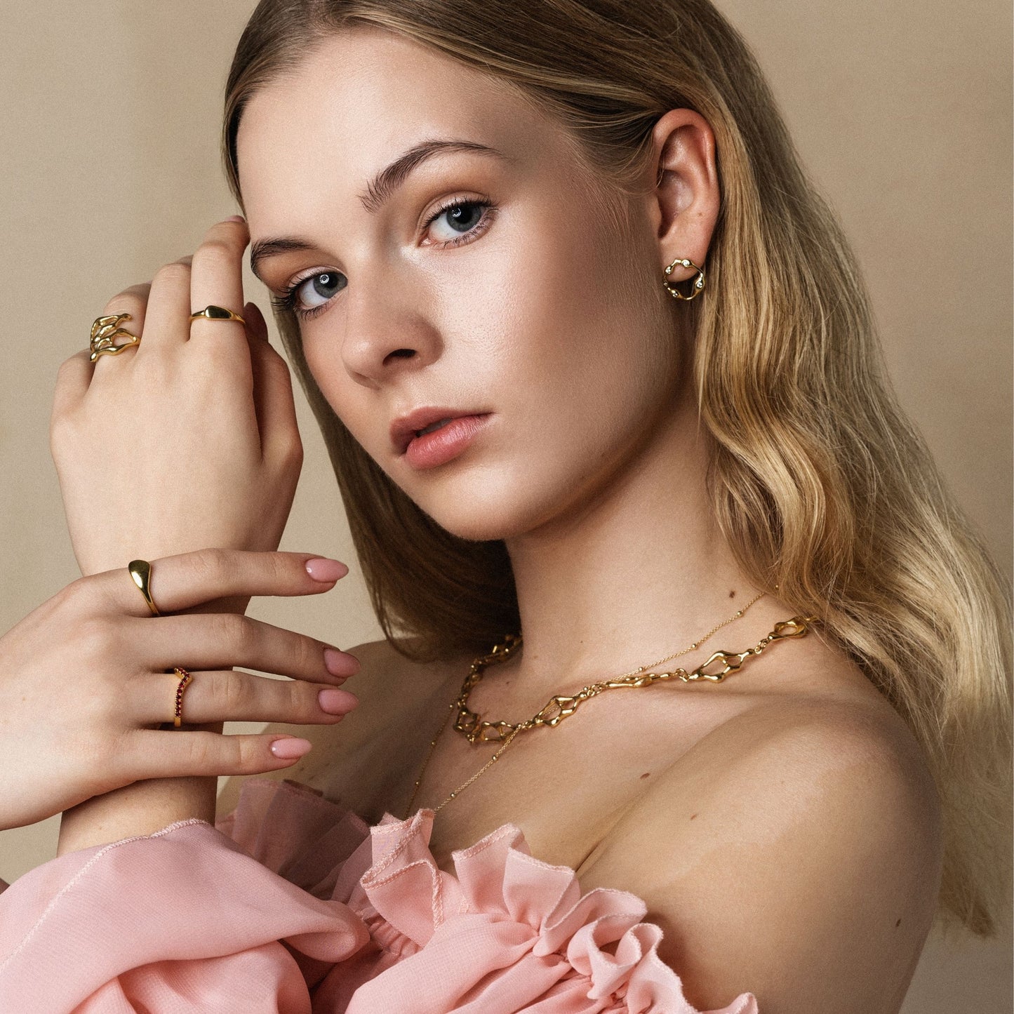 Woman wearing gold jewelry with a pink garment against a beige background