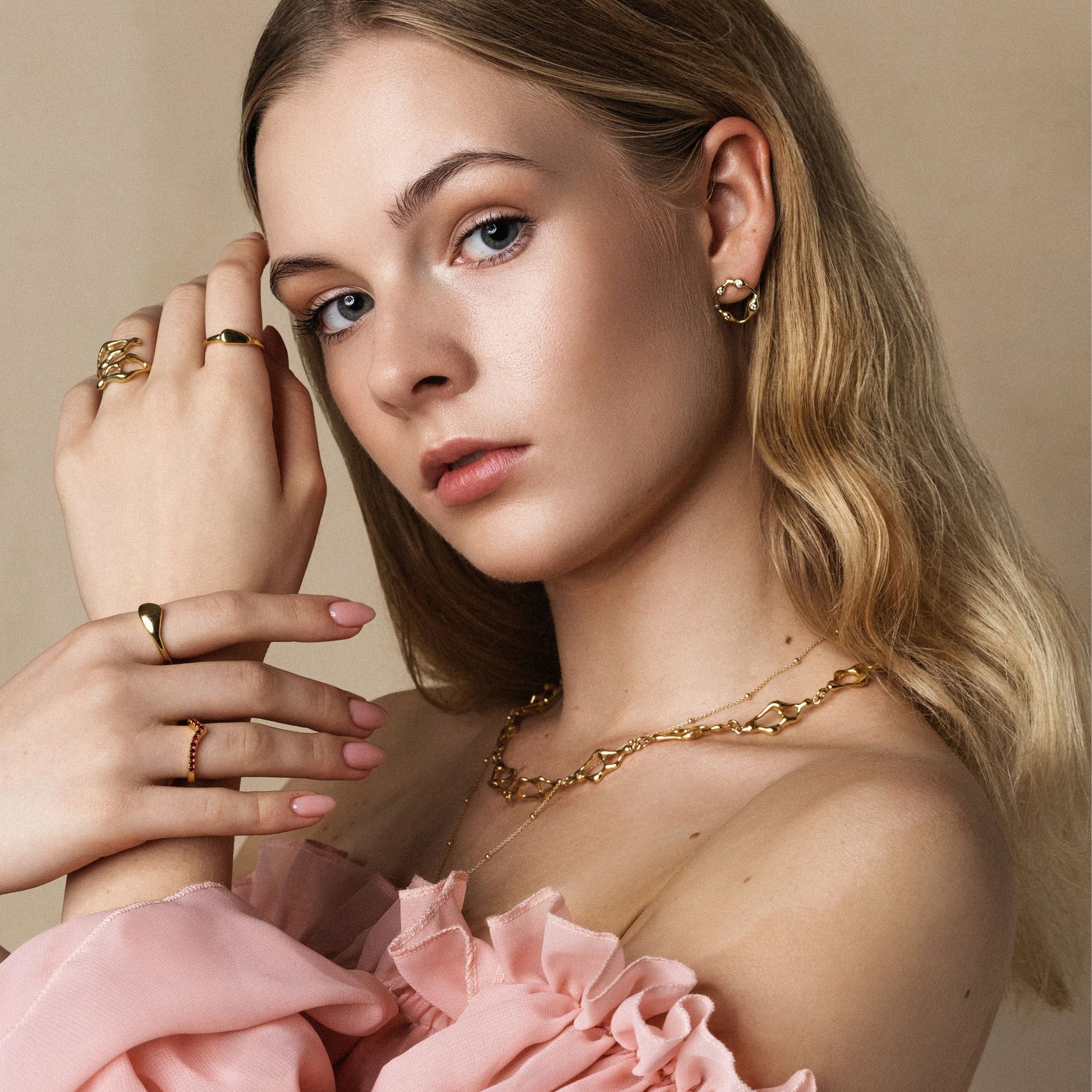 Woman wearing gold jewelry with a pink garment against a beige background