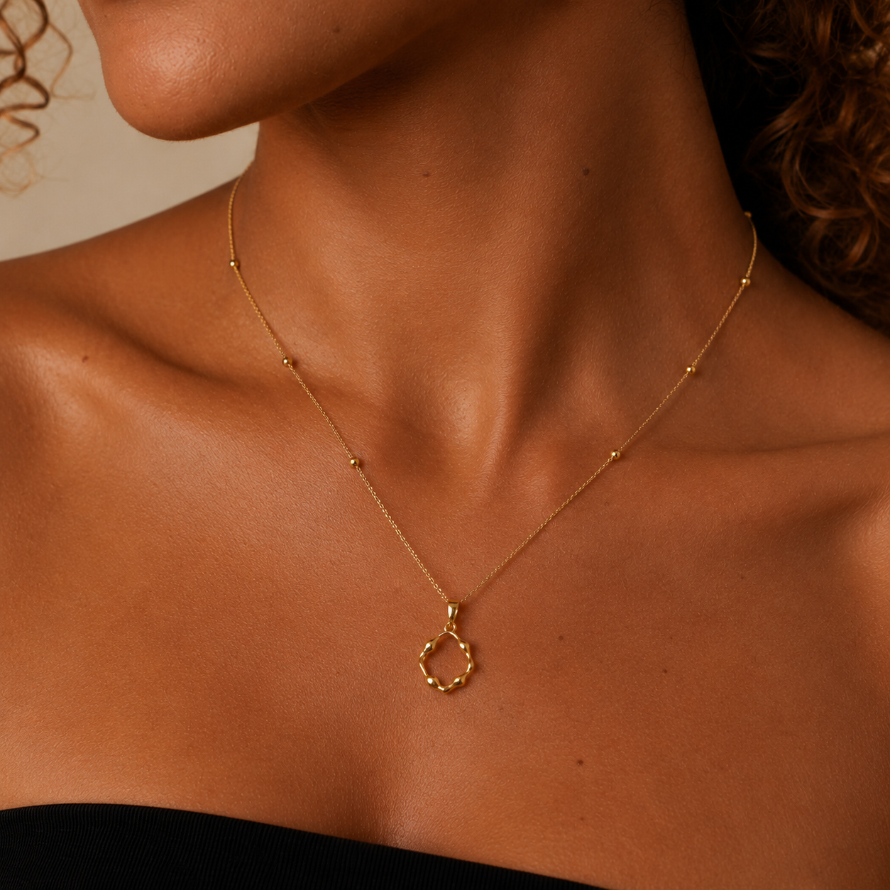 Close-up of a gold necklace with a pendant on a person's neck against a neutral background