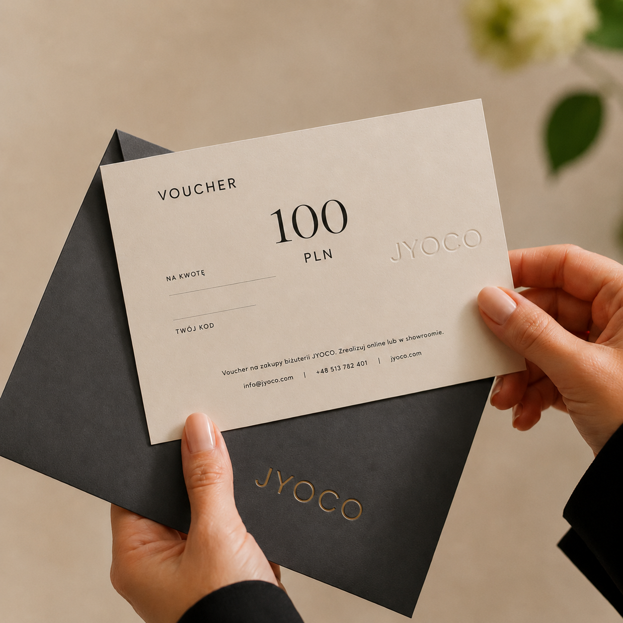 Person holding a JYOCO voucher with 100 PLN inside a black envelope.